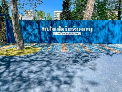 napis Młodzieżowy Ogród Krakowian na niebieskim ogrodzeniu